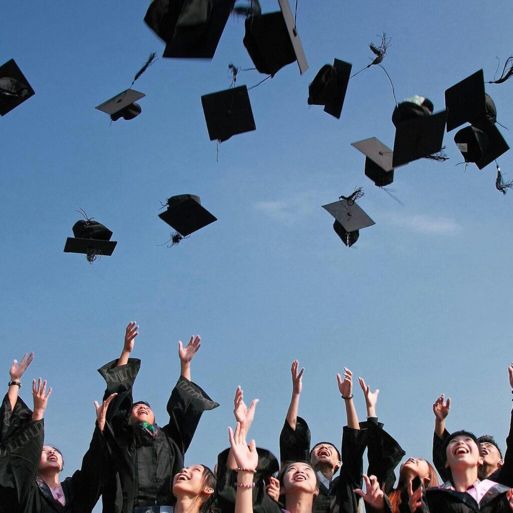 Group of graduates celebrating by throwing caps in the air during a sunny day.